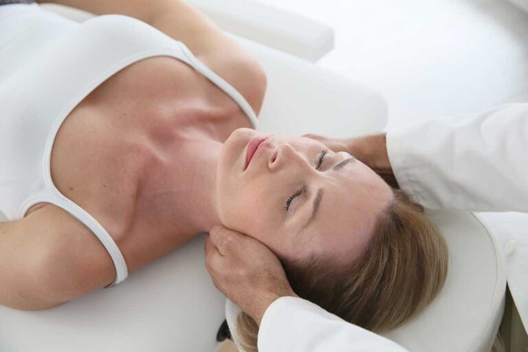 A person carefully rising from bed using their arms for support, with sunlight coming through a nearby window.