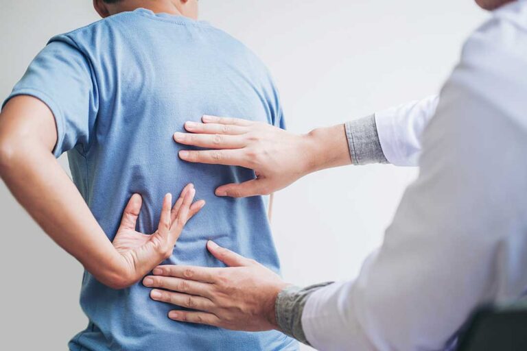 A chiropractor gently adjusting a client's mid-back while discussing symptoms in a quiet treatment room.